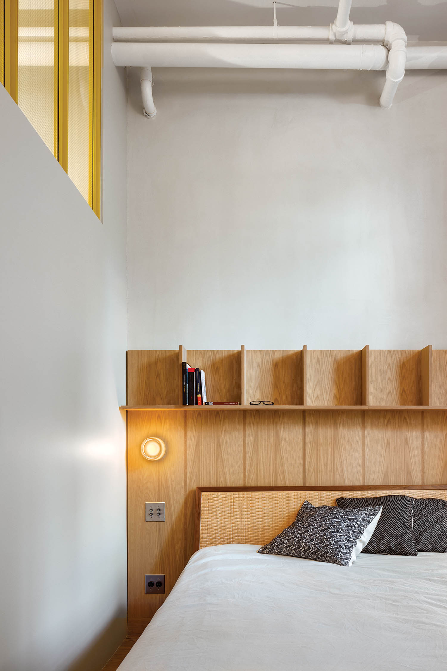 bedroom nook with white sheets, wooden shelf headboard and charcoal pillows