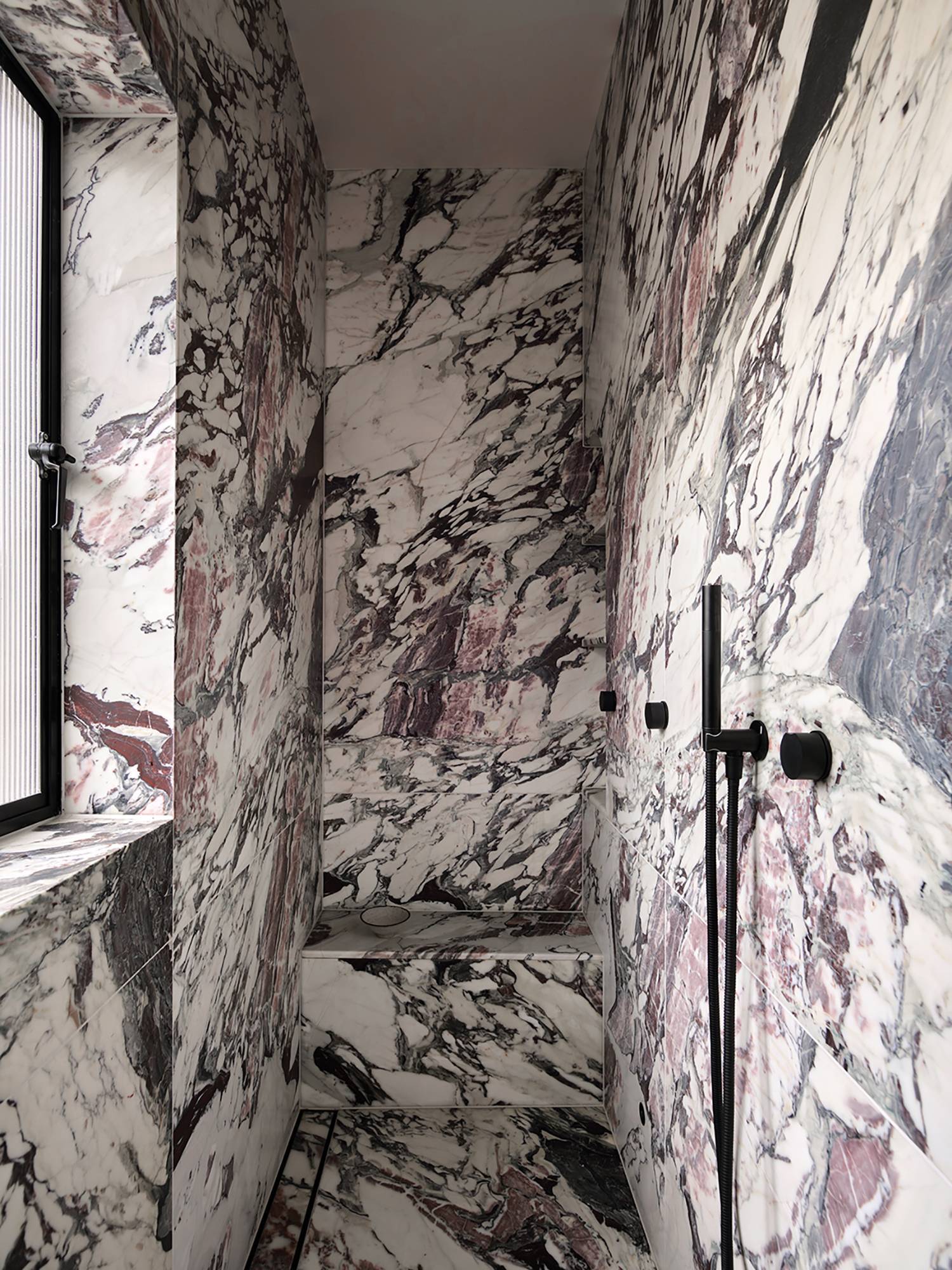 a bathroom with a marble wall and a black and white shower