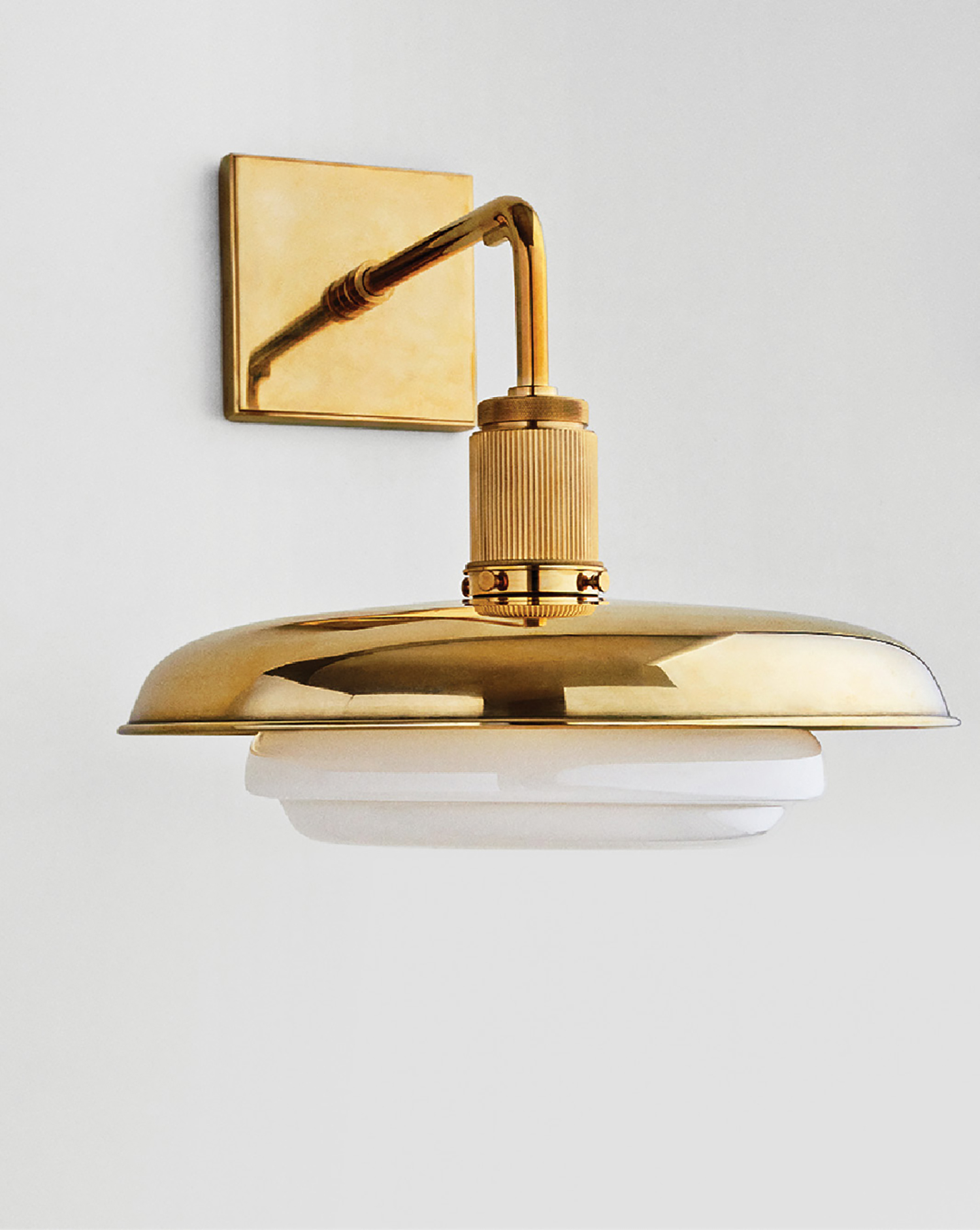 A brass wall light with a white glass shade