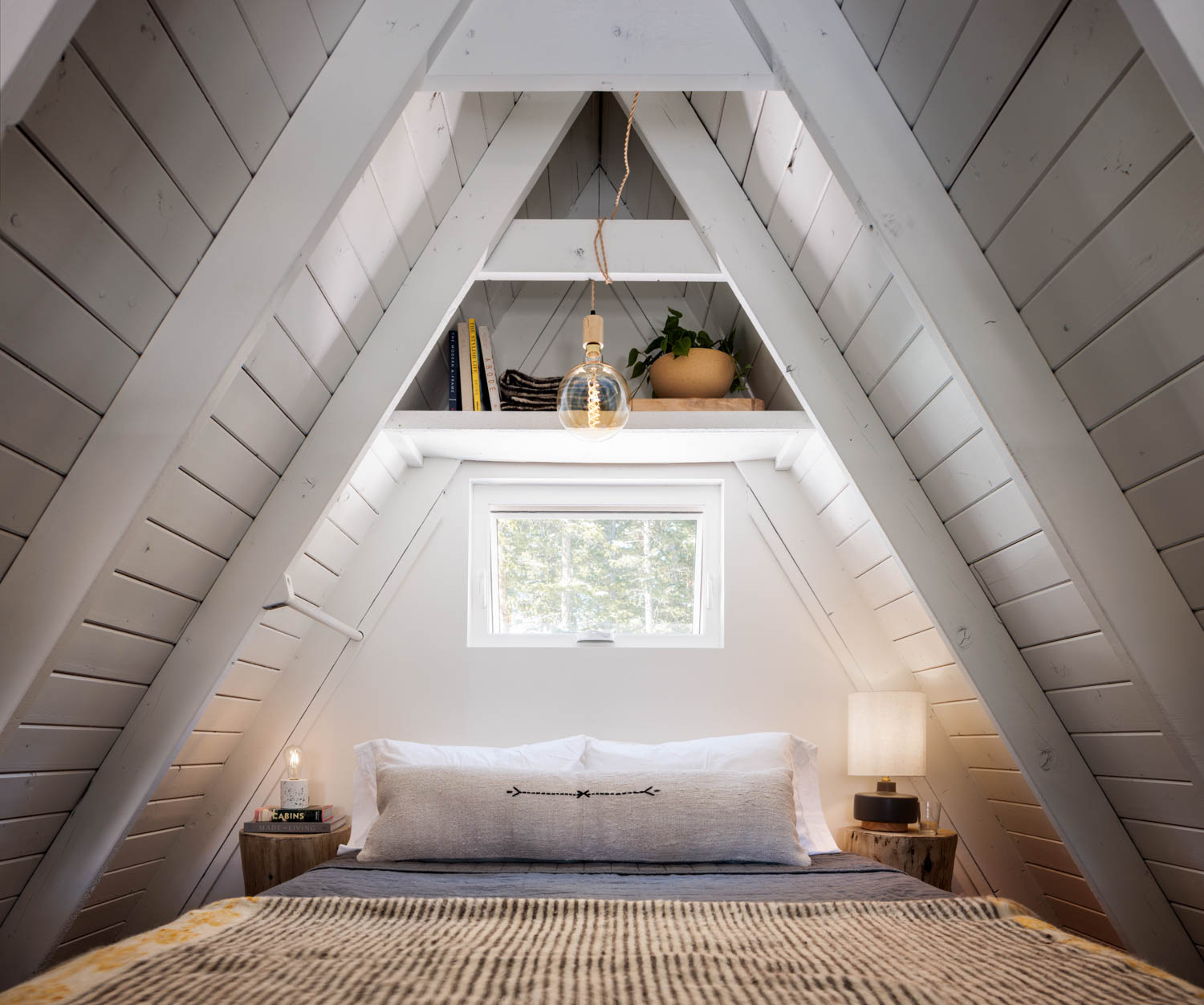 a bed in the loft area of an A-frame ski chalet under a pendant light