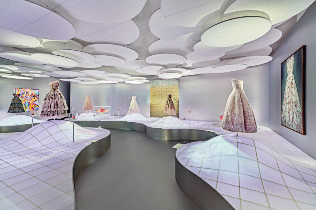 a path snakes around a room with dior dresses on display