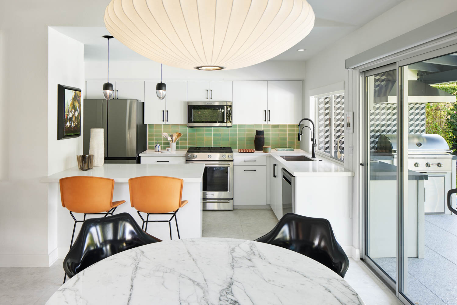 kitchen with green backsplash, orange chairs and white counters