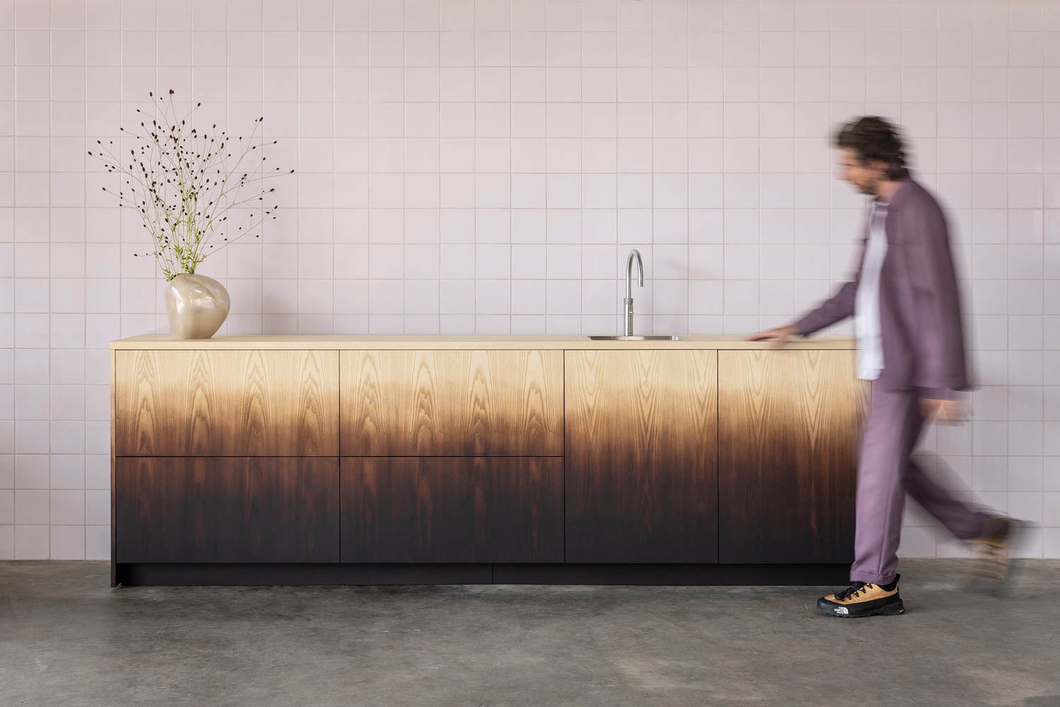 person walking by a cabinet that has an ombre effect from tan to dark brown