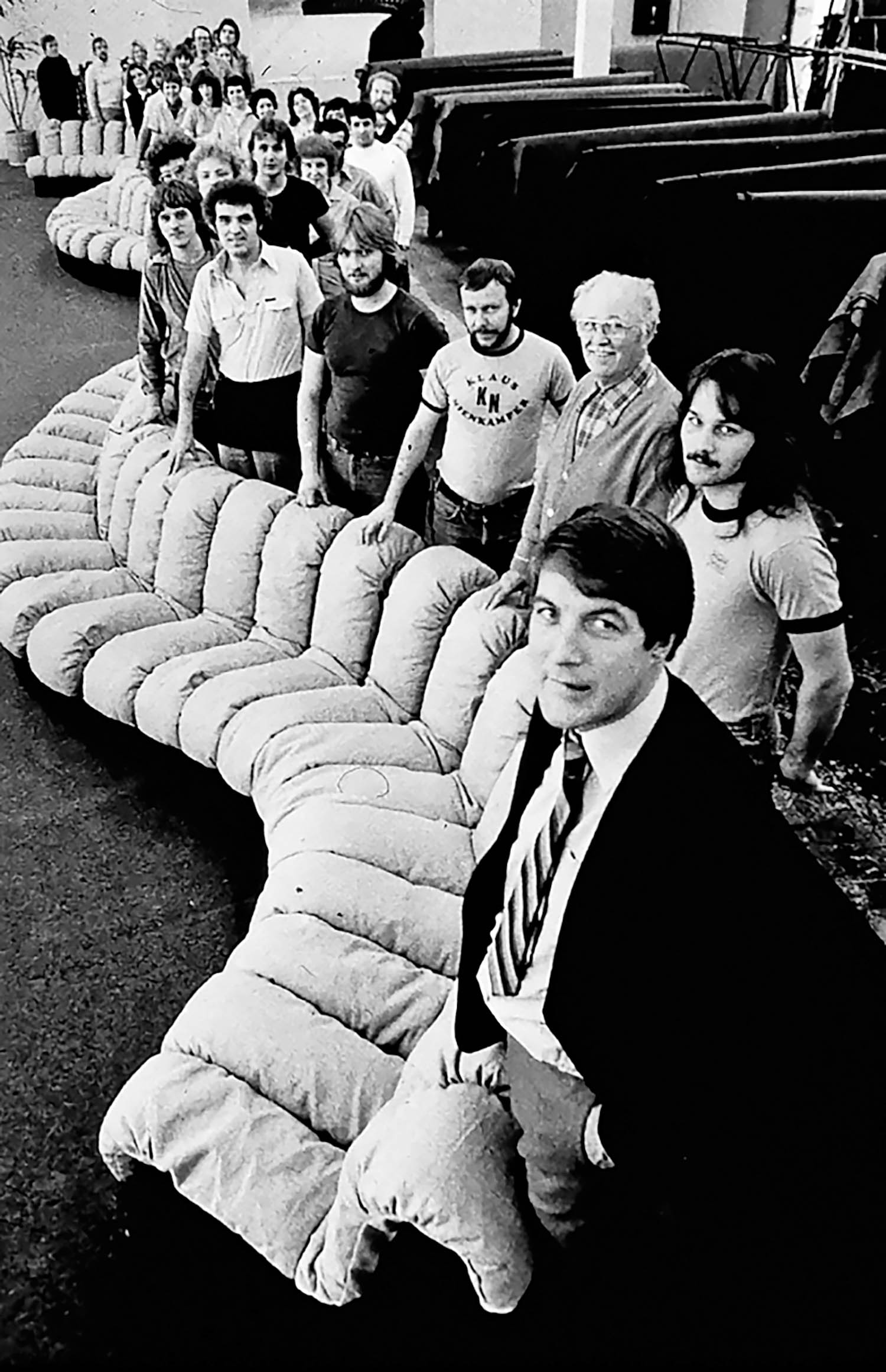 multiple people standing by a long, winding curved sofa