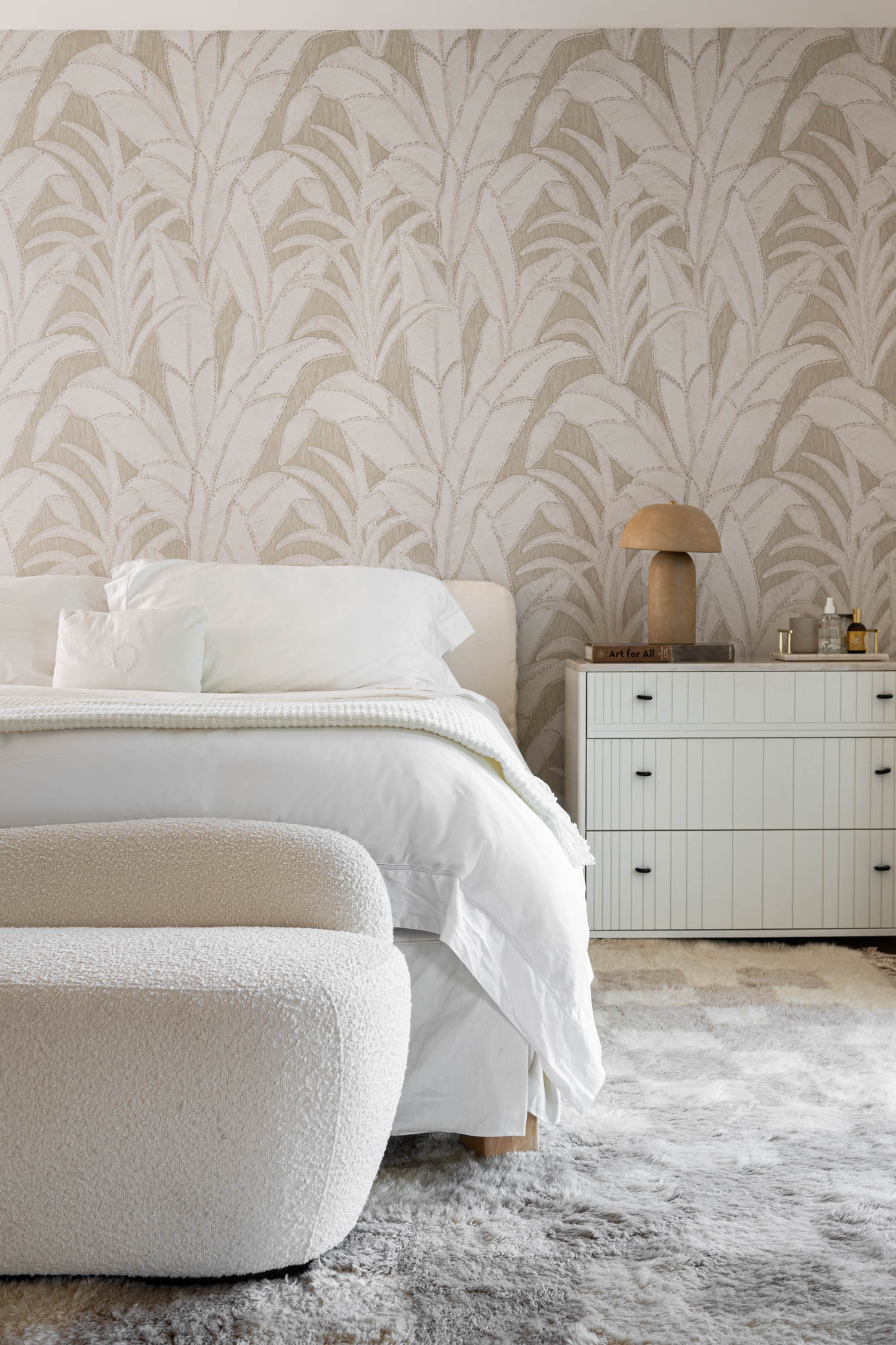 primary bedroom with all white bed, patterned wallpaper with palm trees and patterned rug