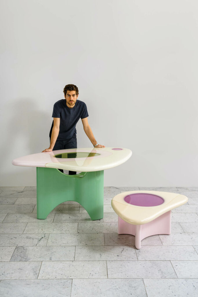 designer leaning on curved tabled with white tops and pastel bases